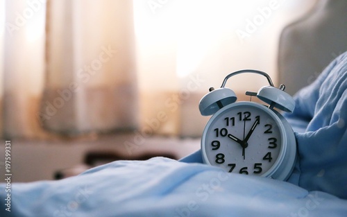 Vintage alarm clock on blue blanket bed closeup sunshine window blur background