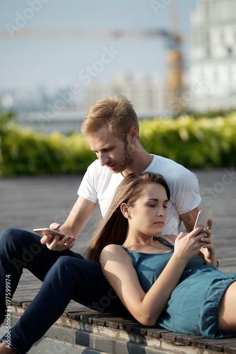 Young couple using smartphones while relaxing together outdoors