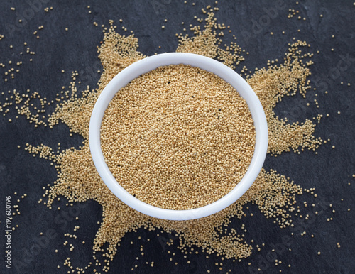 Raw amaranth seeds in a ceramic bowl on a dark shale background, top view, selective focus