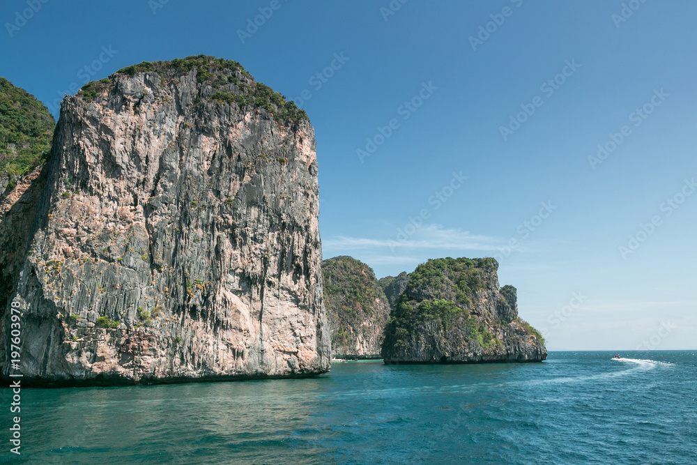 scenic view of rocky formations covered with green plants, blue sky and ocean in phi phi islands