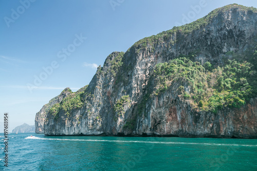 scenic view of rocky formations covered with green plants, blue sky and ocean in phi phi islands