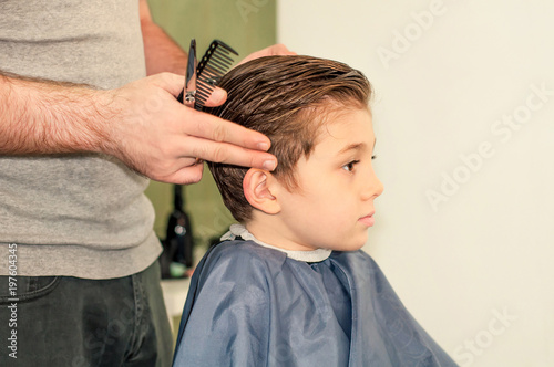Male hands are cutting a pretty boy in a beauty salon.