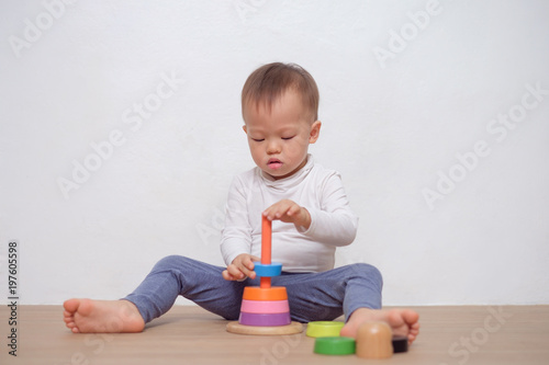 Cute little Asian 18 months / 1 year old toddler baby boy child play with colorful wooden pyramid toy / stacking ring toy. Kid playing with educational toy isolated on white wall, with copy space