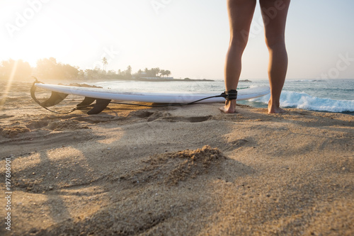 Young woman surfer with surfboard ready to surf. Only leg with leash and sand beach in photo