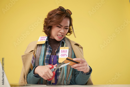Slika na platnu Portrait of angry Asian woman cutting her credit card with scissors to stop spen