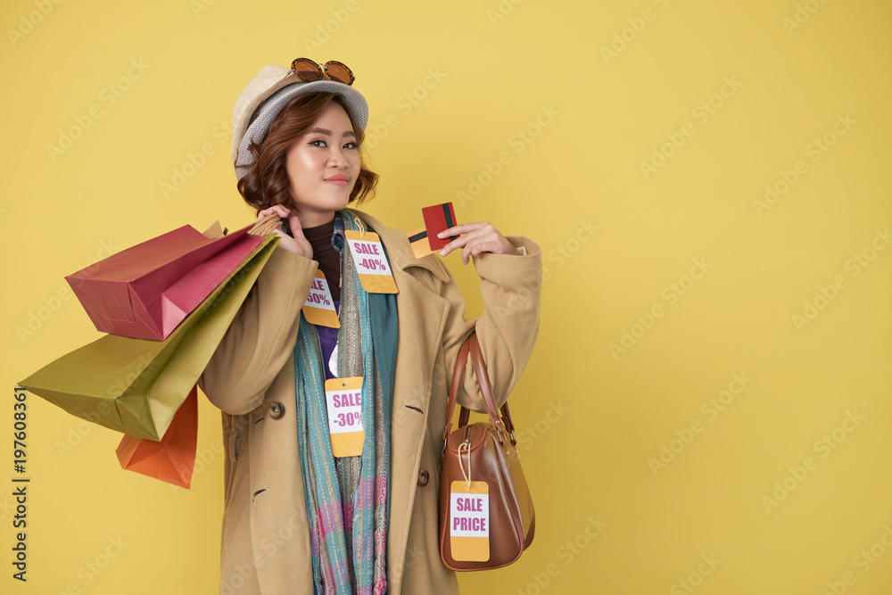 Asian shopaholic woman posing with shopping bags and credit cards after successful shopping, copy space to the right Asian shopaholic woman posing with shopping bags and credit cards after successful shopping, copy space to the right