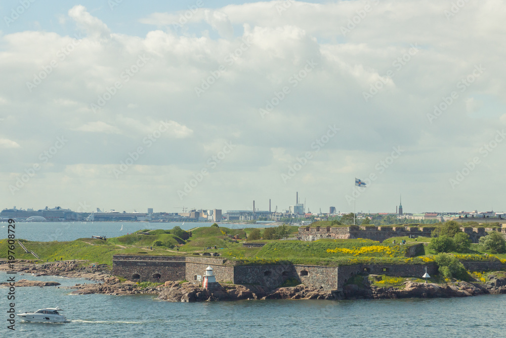 The view from the sea on the covered in green Suomenlinna island with fortifications and fluttering flag, Baltic sea, Finland, Europe