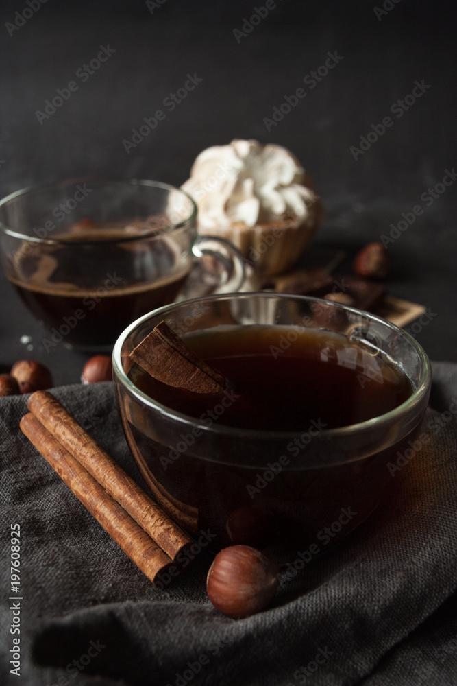 Close-up. Transparent cup of coffee, cinnamon sticks on a grey linen napkin. Dark background Close-up. Transparent cup of coffee, cinnamon sticks on a grey linen napkin. Dark background