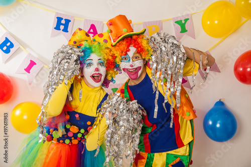 Clown girl and clown boy in bright costumes at the baby's birthday party. The explosion of emotions and the fun of the circus. Paper disco made of silver paper
