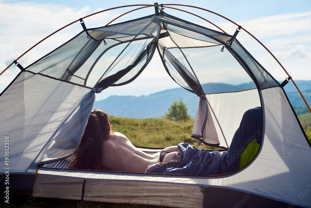 Fotka „Back view of attractive naked female traveller lying in tent in sleeping bag, enjoying summer day in the mountains. Camping lifestyle concept“ ze služby Stock | Adobe Stock