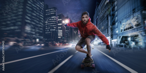 Hipster man rides on a longboard in the streets at night