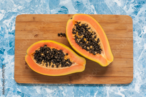 The cut papaya lies on a wooden background. The two halves of the exotic fruit photo