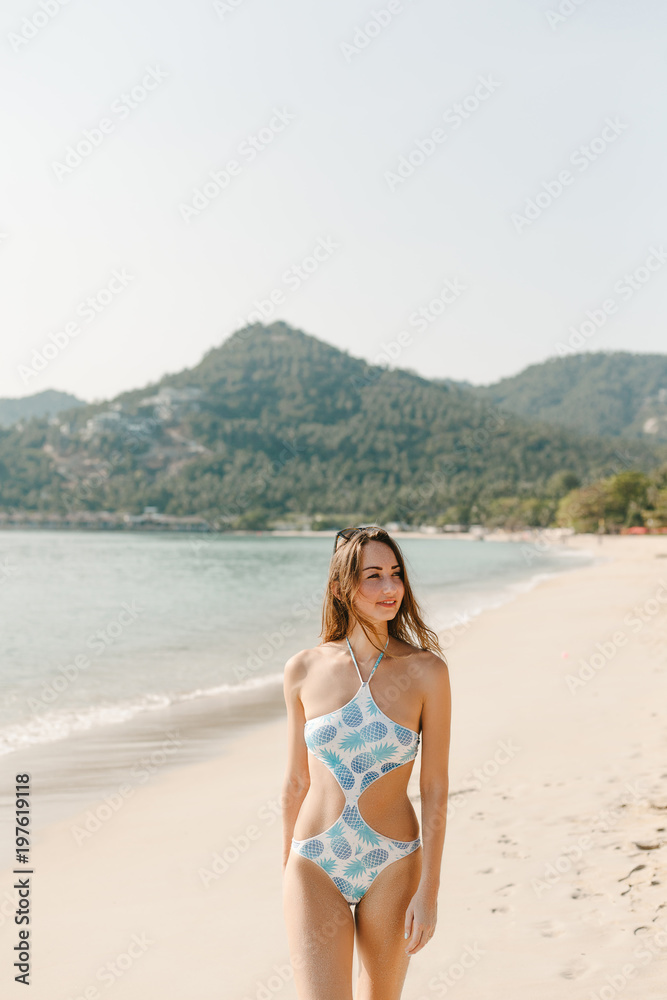 beautiful woman posing in swimsuit on beach on tropical resort