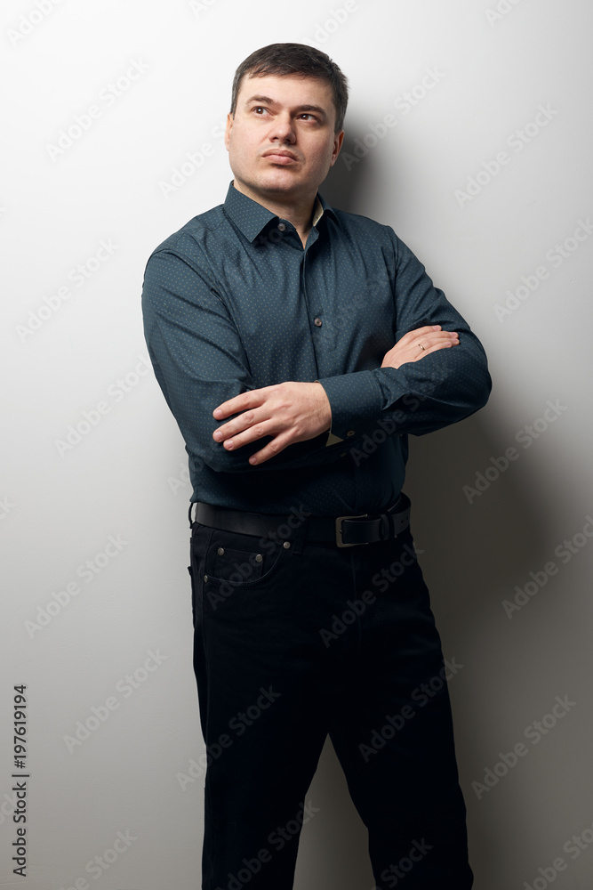 man portrait with crossing hands, dressed in dark shirt and black pants over gray background