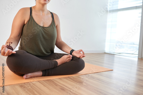 Close-up shot of unrecognizable young woman sitting in lotus position and meditating while having training at modern health club