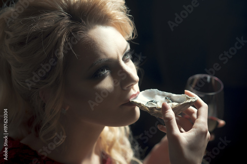 oyster dinner. Beautiful sexy fashion brunette woman in expensive interior restaurant eat oyster and lick one finger on dark cafe background