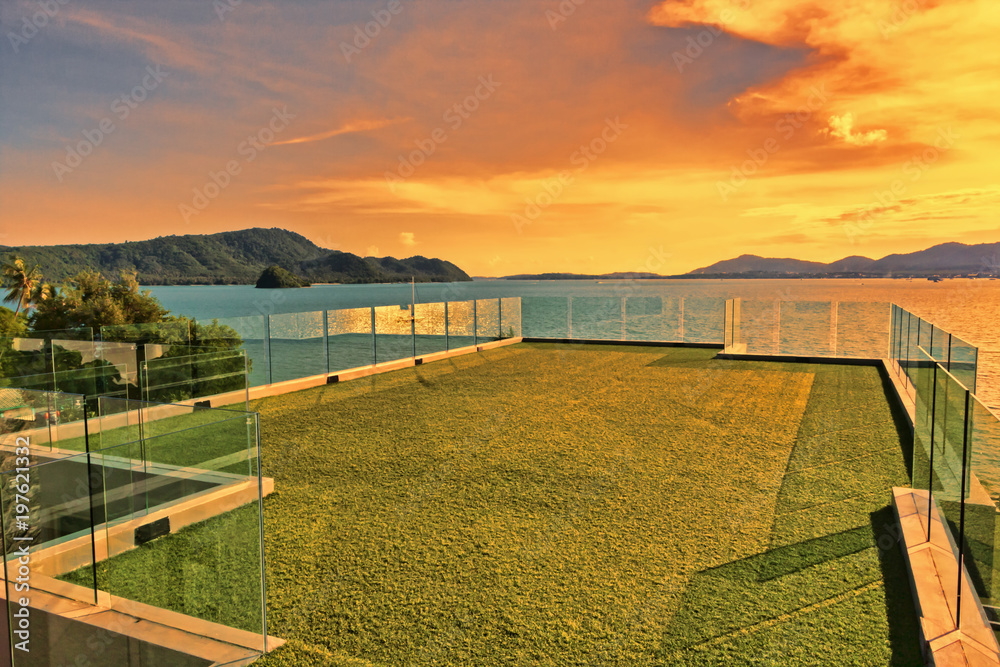 Luxurious lawn green terrace overlooking  ocean and  tropical golden sunset