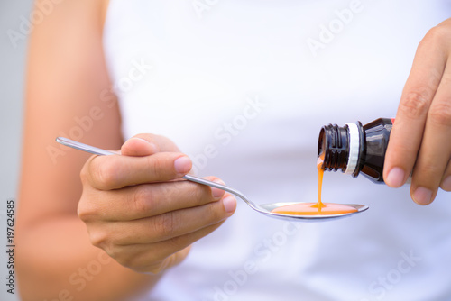 Woman pouring medication or antipyretic syrup from bottle to spoon. healthcare, people and medicine concept. photo