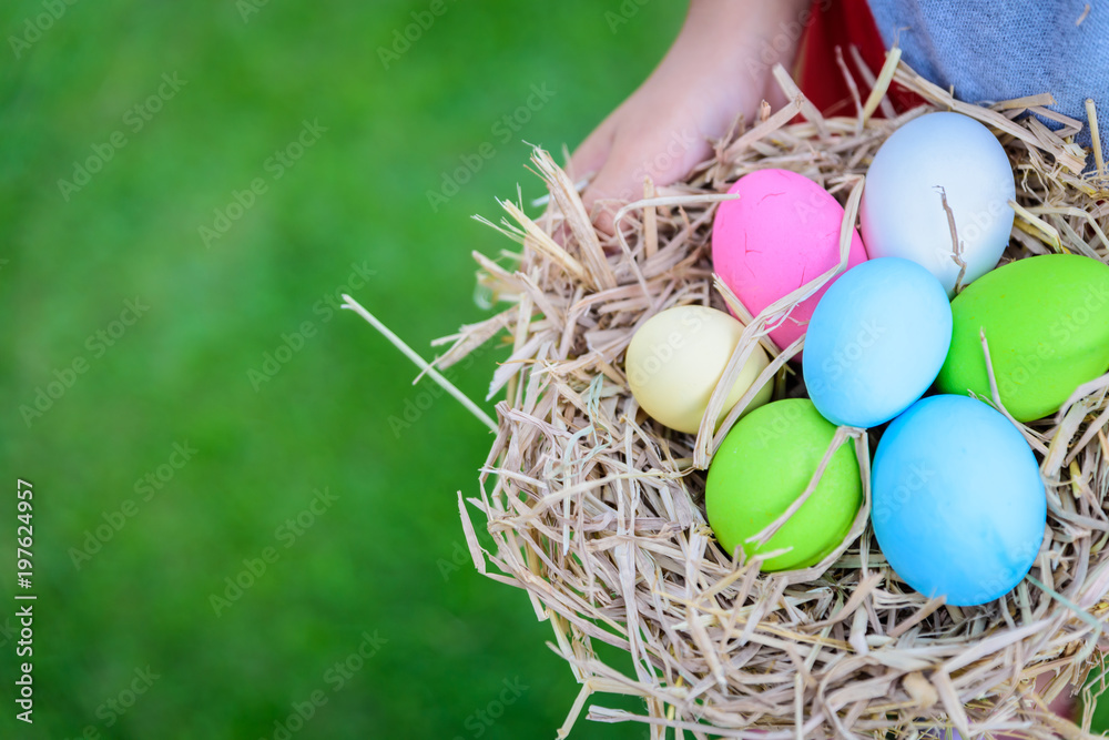 Obraz premium A kid holding Colorful of Easter eggs in nest on grass green background.