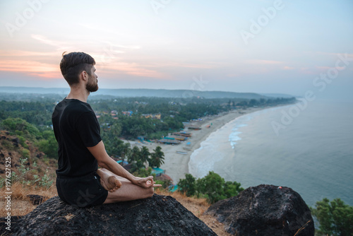 Healthy man practicing yoga under the beach at sunset.