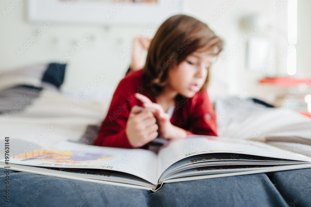 young boy reading a book at home on the bed young boy reading a book at home on the bed