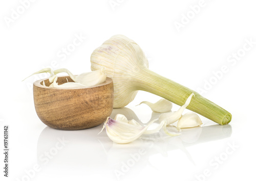 Young garlic separated cloves in a wooden bowl and one bulb with green stem isolated on white background.