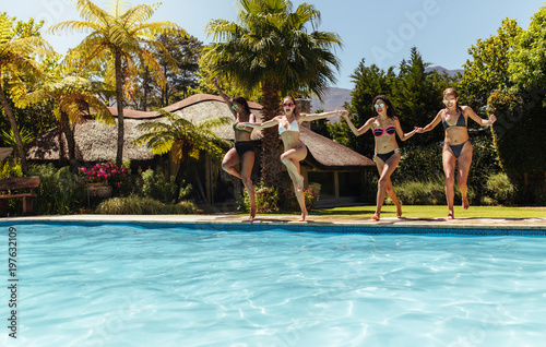 Women friends jumping in the swimming pool