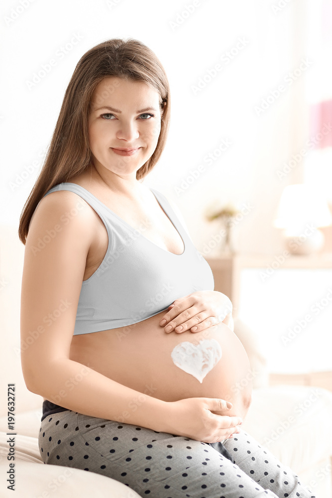 Pregnant woman with heart painted on her belly against blurred background Pregnant woman with heart painted on her belly against blurred background