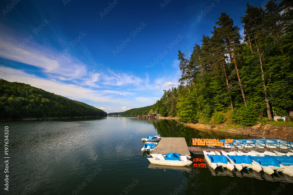 Mountain landscape with docks and pedal cycle boats on lake Gozna surrounded by forest at Valiug, Caras-Severin County, Romania