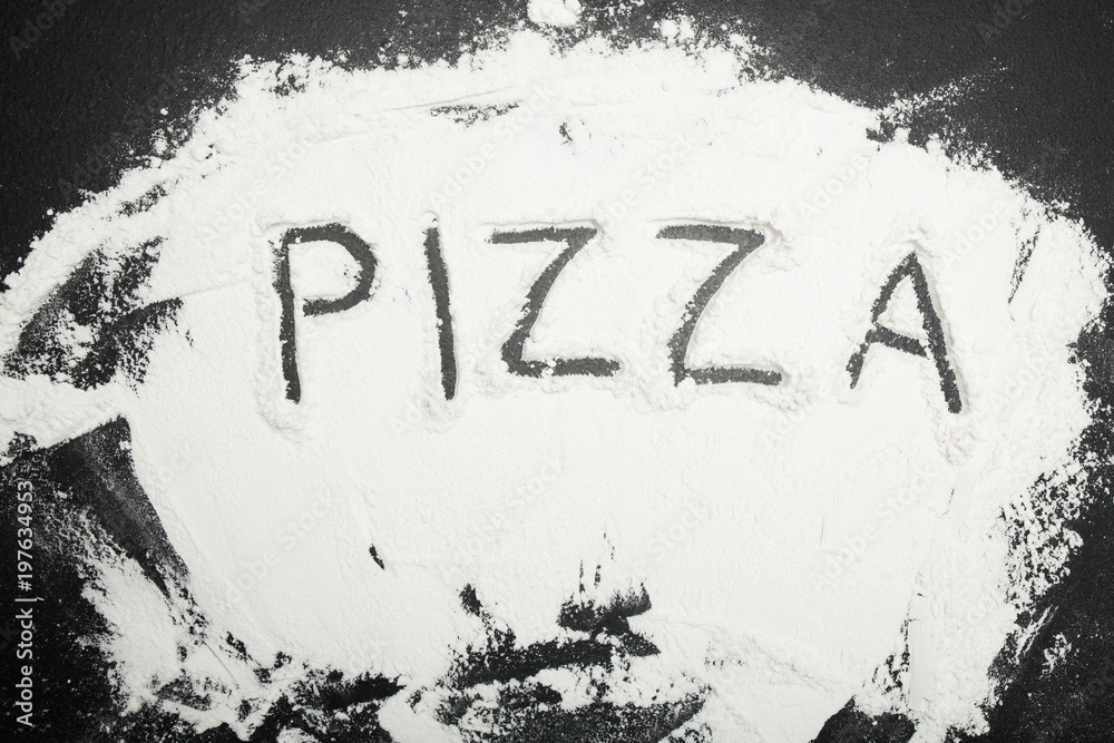 White flour on a black table, inscription pizza. White flour on a black table, inscription pizza.