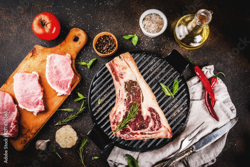 Raw beef marbled meat striplon rib eye steak with pork steaks, spices, grill pan, and herbs, dark background top view, copy space