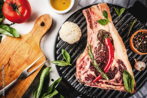 Raw beef marbled meat striplon rib eye steak with spices, grill pan, and herbs, white marble background top view, copy space photo