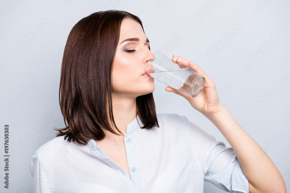 Side view profile of pretty, charming, stylish woman with modern hairstyle in casual outfit having glass with water, drinking, enjoying with close eyes, isolated on grey background Side view profile of pretty, charming, stylish woman with modern hairstyle in casual outfit having glass with water, drinking, enjoying with close eyes, isolated on grey background