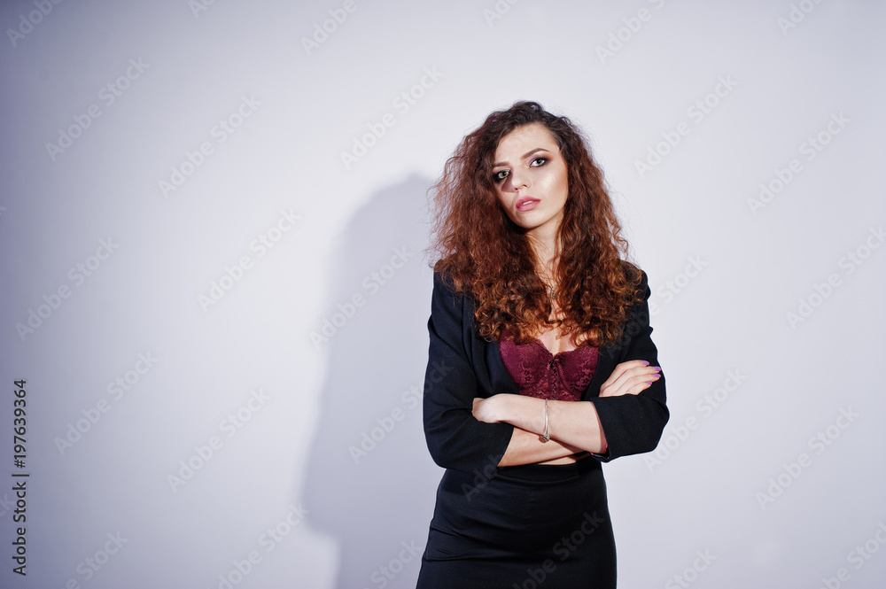 Brunette curly haired girl in black office jacket with skirt, on bra at studio against white background. Sexy businesswoman.