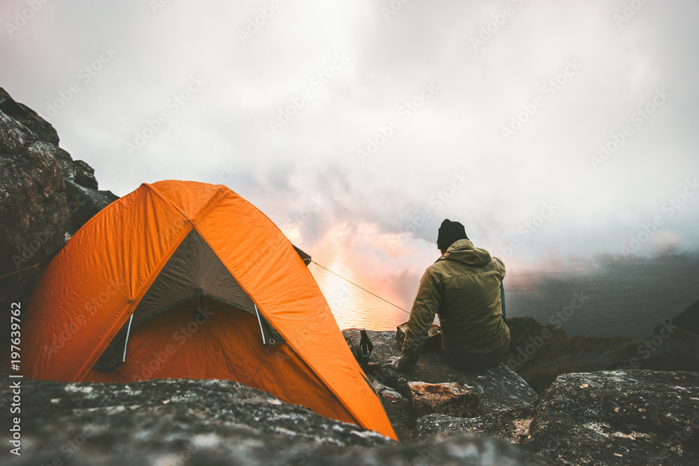 Man traveler alone enjoying sunset in mountains sitting near of tent camping gear outdoor Travel adventure lifestyle concept hiking wanderlust vacations - obrazy, fototapety, plakaty 