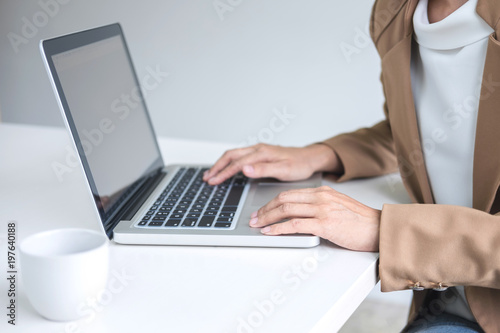 Young Entrepreneur woman manager working indoors at a modern office, typing and holding a coffee cup while using her laptop