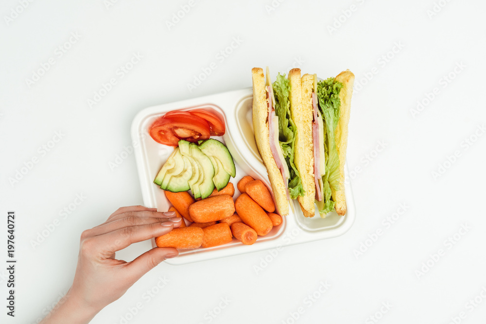 cropped image of woman taking carrot from lunch box isolated on white