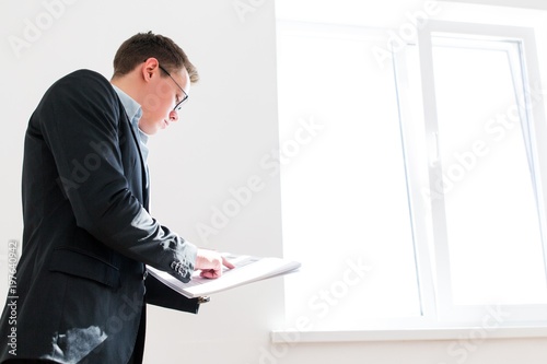 Businessman With glasses showing his finger on the building drawing standing indoors