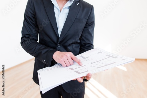 Businessman pointing his finger at the blueprint standing in an empty room