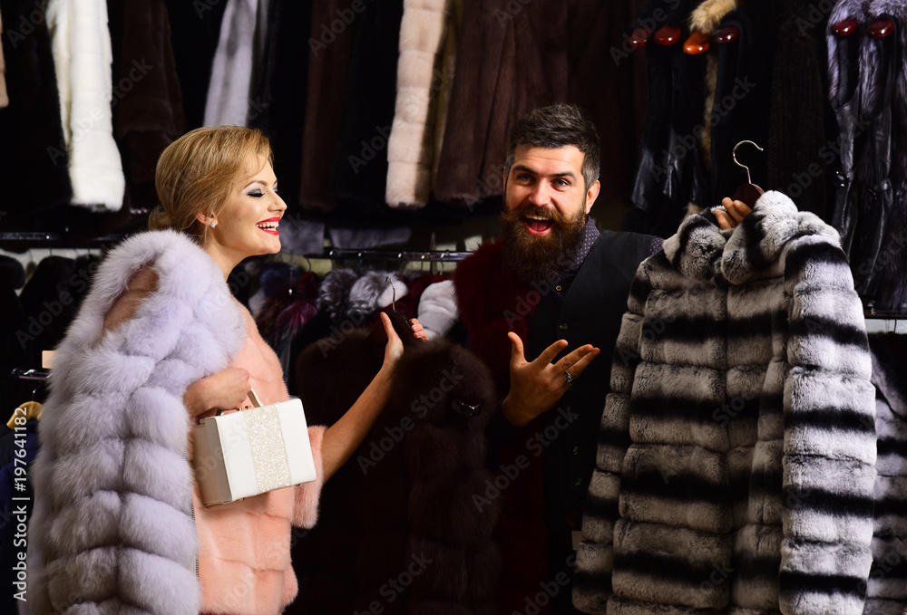 Shop assistant with beard shows fur coat to lady.