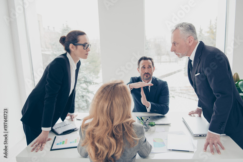 Two stylish business persons in suits having disagreement, war, conflict, standing near desktop in front of each other, face to face with disrespect expression, partner showing stop sign with hands photo