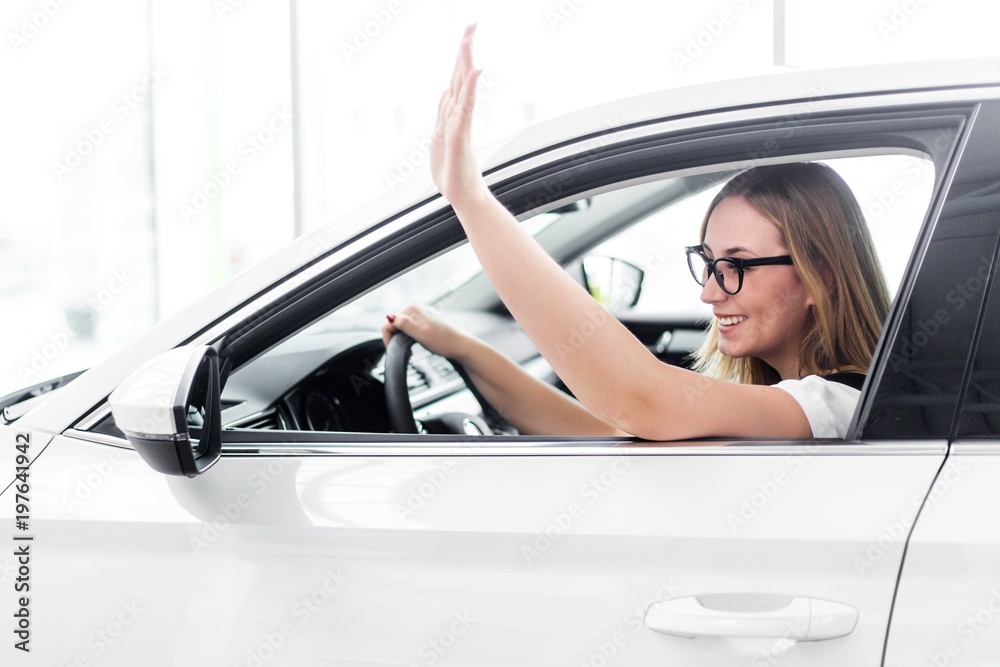 Attractive girl waving her hand sitting behind the wheel of a car