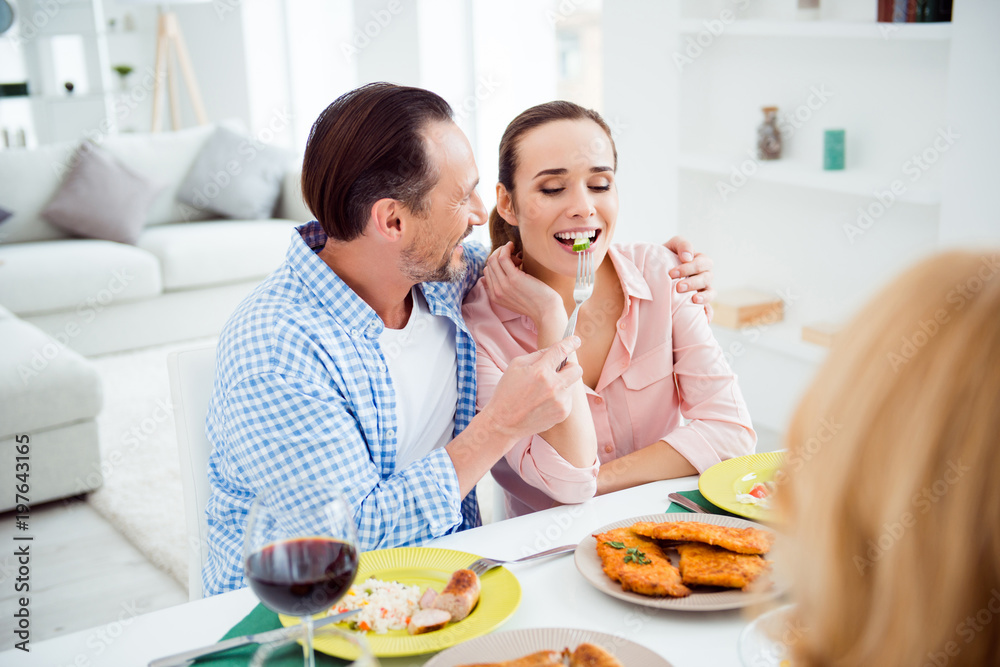 Portrait of attractive, cute, sweet, lovely, festive, cheerful couple sitting with friends in house, apartment, room, visiting parents, men feeding his woman, giving food with fork, having fun