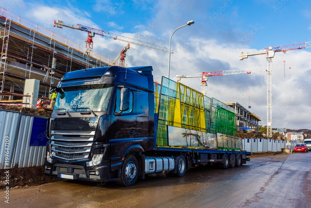 Construction site with crane and building against blue sky. Black truck with window glass Construction site with crane and building against blue sky. Black truck with window glass