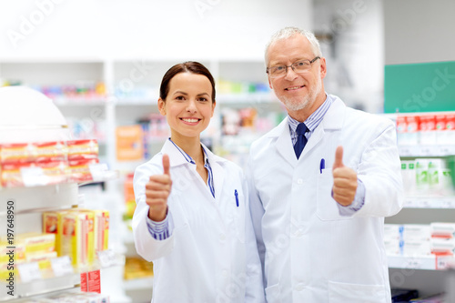 medicine, healthcare and technology concept - happy smiling apothecaries at pharmacy showing thumbs up