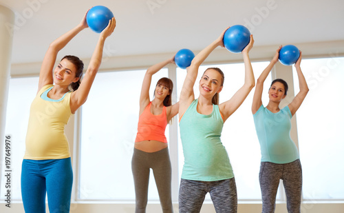 pregnancy, sport, fitness and healthy lifestyle concept - group of happy pregnant women training with small exercise balls in gym