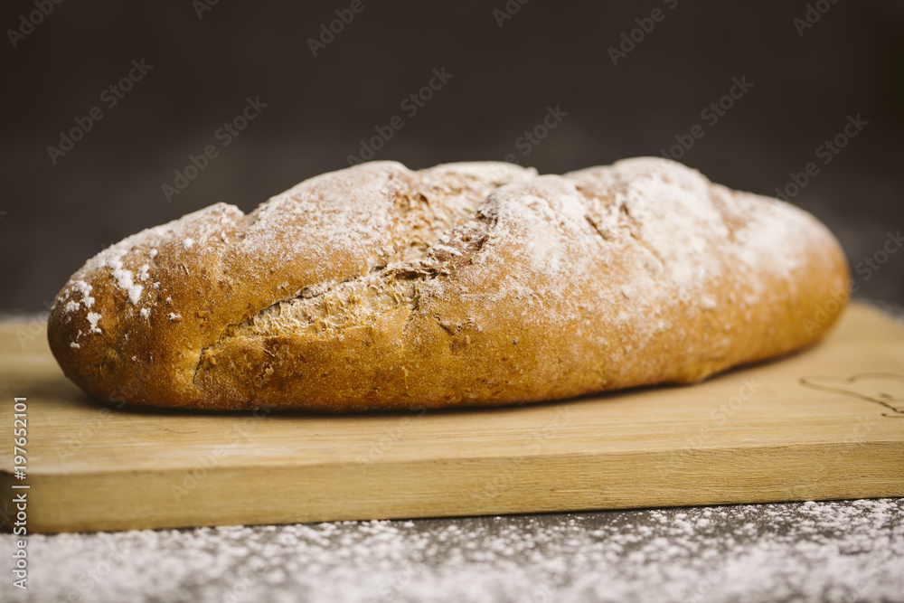 Fresh bread on dark wood with sprinkled flour.