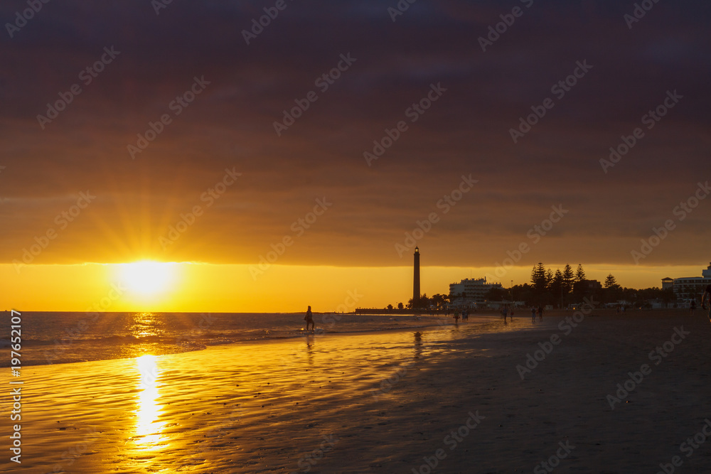 Walker on seashore with lighthouse during sunset in Maspalomas, Gran Canaria Island. Walker on seashore with lighthouse during sunset in Maspalomas, Gran Canaria Island.