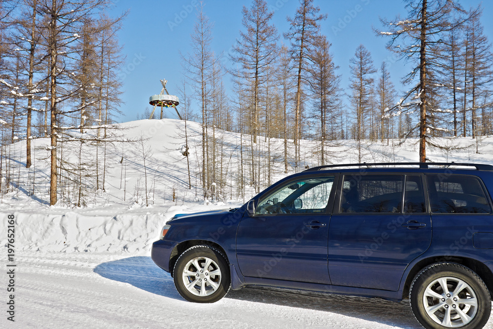 Car crosses the line of northern polar circle along  winter road near the sign 