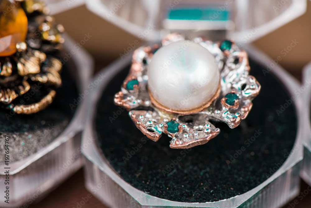 Macro shot of silver engagement ring in gift box on colorful, sparkling background. Gemstone ring made of pearl, sapphire crystals and  apatite gemstones. 